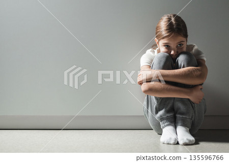 Vulnerable child curled up against gray wall feeling despair stress needs for protection Vulnerable child curled up against gray wall feeling despair stress needs for protection 135596766