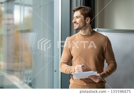 Positive young man standing near the flipchart in the office and presenting a new project 135596875