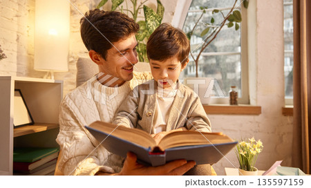 Father and son reading together on armchair. 135597159