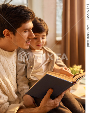 Father and son sharing bedtime reading moment in cozy living room. 135597161