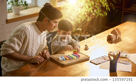 Father and son playing with modeling clay at wooden table. 135597191