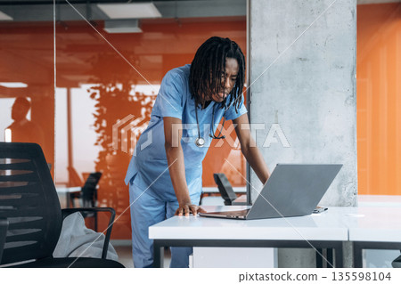 Silver colored laptop is on the table. Black man doctor is in the office 135598104