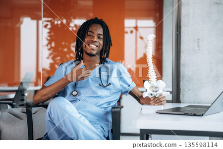 Holding and showing model of human spine. Black man doctor is in the office Holding and showing model of human spine. Black man doctor is in the office 135598114