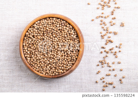 Coriander seeds, whole and dried, in a wooden bowl on linen. Fruits of Coriandrum sativum, a spice with lemony citrus flavor, due to the terpenes linalool and pinene, that enhances when roasted. Photo 135598224