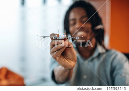 Focused view of toy plane, airline company. Black businessman is working in office Focused view of toy plane, airline company. Black businessman is working in office 135598243