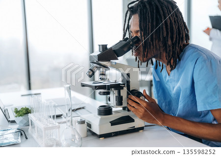 The microscope on the table. Black man doctor is in the office The microscope on the table. Black man doctor is in the office 135598252