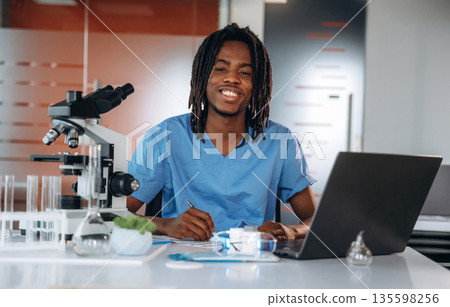 The microscope on the table. Black man doctor is in the office The microscope on the table. Black man doctor is in the office 135598256