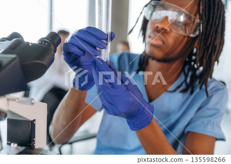 In protective eyewear, with microscope. Black man doctor is in the office 135598266