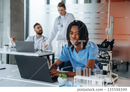 Guy is working by laptop. Doctors are in the clinic Guy is working by laptop. Doctors are in the clinic 135598399