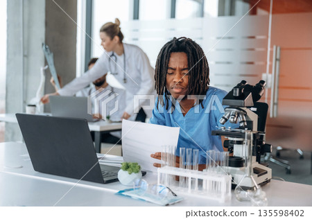 Guy is working by laptop. Doctors are in the clinic 135598402