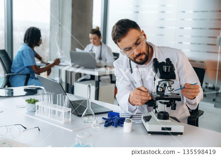 In lab coat, sitting with microscope. Doctors are in the clinic 135598419