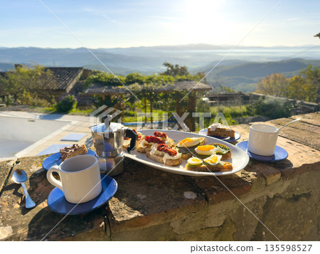 Outdoor breakfast with coffee cups moka pot toast eggs vegetables and hillside view 135598527