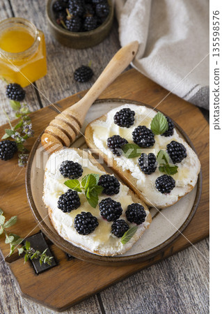 A rustic breakfast scene features bread slices topped with fresh blackberries and cream, garnished with mint leaves.  135598576