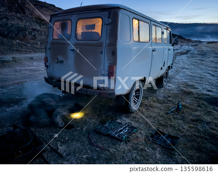 Old van being repaired in remote field at dusk with tools and mechanic 135598616