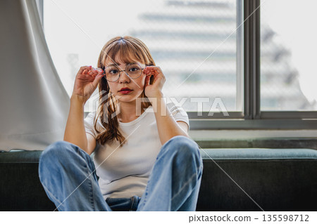 一位戴著圓框眼鏡的女士正在窗邊放鬆。 135598712