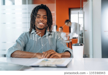 Guy is in front of his colleagues, sitting. People are working in the office together Guy is in front of his colleagues, sitting. People are working in the office together 135598943