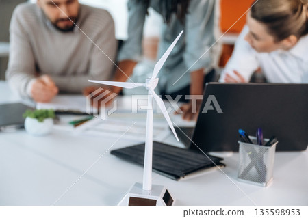 Green energy, model of wind turbine. People are working in the office together Green energy, model of wind turbine. People are working in the office together 135598953