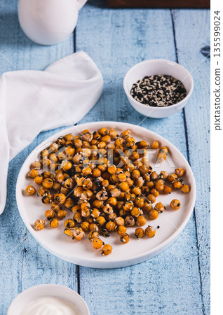 Appetizing roasted chickpeas with sesame seeds and herbs on a plate on the table vertical view Appetizing roasted chickpeas with sesame seeds and herbs on a plate on the table vertical view 135599024