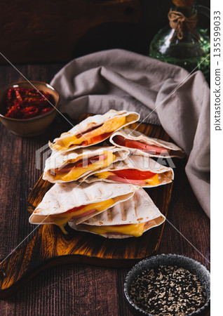 Sausage, tomatoes and cheese wrapped in flat grilled bread on a board on a table vertical view Sausage, tomatoes and cheese wrapped in flat grilled bread on a board on a table vertical view 135599033