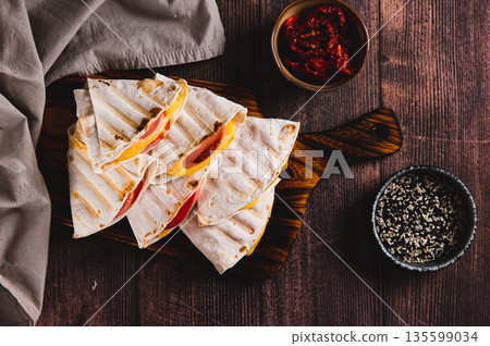 Grilled sandwiches with sausage, cheese and tomatoes in a tortilla on a board on a table top view Grilled sandwiches with sausage, cheese and tomatoes in a tortilla on a board on a table top view 135599034