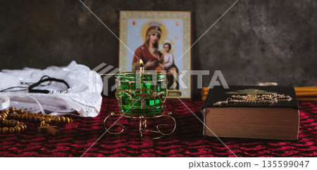 A burning Orthodox lamp, a Bible, a cross with a chain, and an icon on the table web banner 135599047