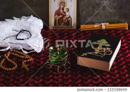 A lamp, rosary beads, a Bible, an Orthodox icon and a cross for prayer on a red table 135599049