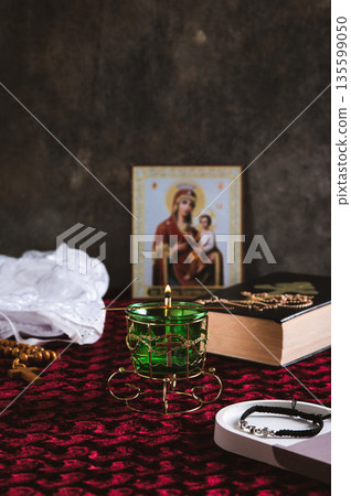 A burning Orthodox lamp, a Bible, a cross with a chain, and an icon on the table vertical view A burning Orthodox lamp, a Bible, a cross with a chain, and an icon on the table vertical view 135599050
