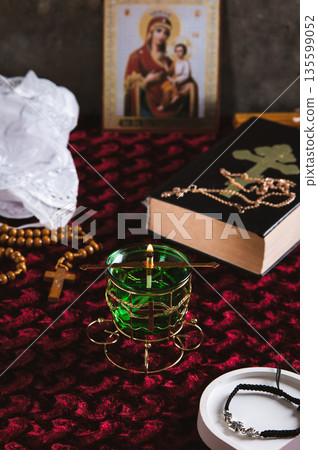 A lamp, rosary beads, a Bible, an Orthodox icon and a cross for prayer on a red table vertical view 135599052