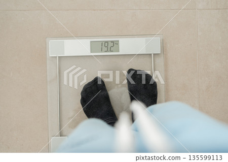 Top view of person checking weight on digital bathroom scale. Concept of health monitoring, diet progress and lifestyle balance Top view of person checking weight on digital bathroom scale. Concept of health monitoring, diet progress and lifestyle balance 135599113