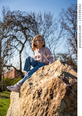 Little girl jumping on decorative stones in city park. Active spring play and outdoor childhood lifestyle. 135599162