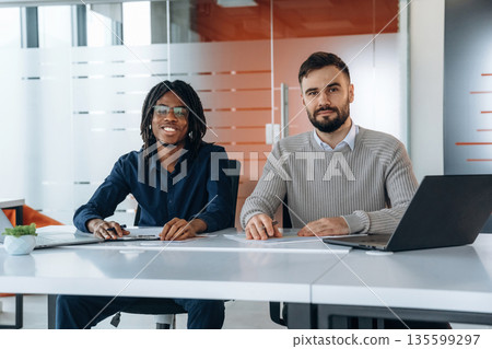Looking at the camera, sitting. Two men are working in the office Looking at the camera, sitting. Two men are working in the office 135599297