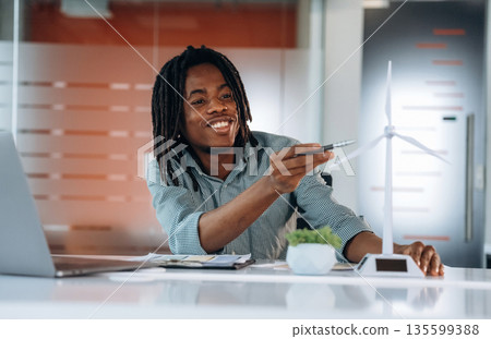 Wind turbine, little model, company. Black businessman is working in office 135599388