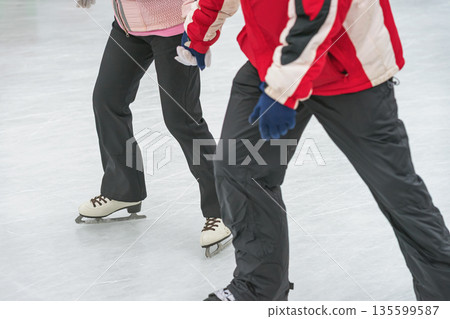 Two people holding hands while ice skating together on winter rink. Concept of shared skating experience, active date skating, friendship, seasonal winter sport Two people holding hands while ice skating together on winter rink. Concept of shared skating experience, active date skating, friendship, seasonal winter sport 135599587