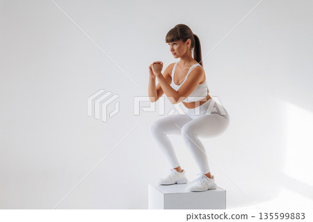 Doing squats. Young sportive woman is in the studio 135599883