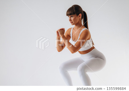 Doing squats. Young sportive woman is in the studio 135599884