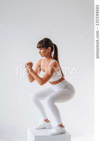 Doing squats. Young sportive woman is in the studio Doing squats. Young sportive woman is in the studio 135599885