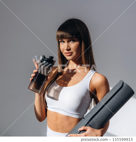 Taking a break, with bottle of water. Young sportive woman is in the studio Taking a break, with bottle of water. Young sportive woman is in the studio 135599913