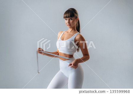 Measuring the waist. Young sportive woman is in the studio 135599968
