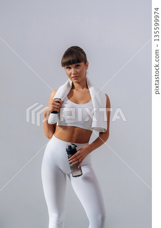 Against white wall. Young sportive woman is in the studio Against white wall. Young sportive woman is in the studio 135599974