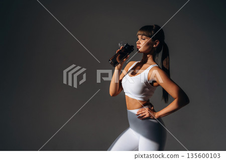 Drinking water, break. Young sportive woman is in the studio 135600103