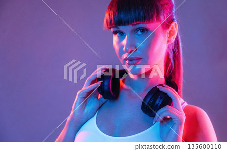 Headphones on the neck. Young sportive woman is in the studio 135600110