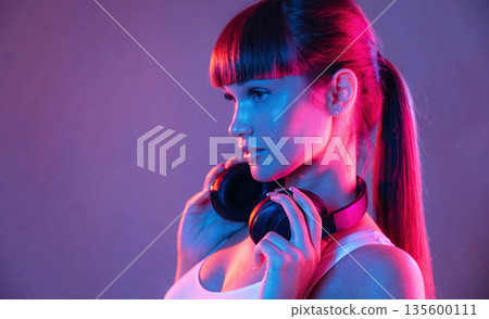 Headphones on the neck. Young sportive woman is in the studio 135600111