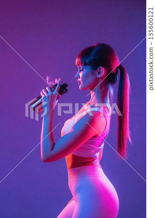 Remember to hydrate, holding bottle of water. Young sportive woman is in the studio Remember to hydrate, holding bottle of water. Young sportive woman is in the studio 135600121