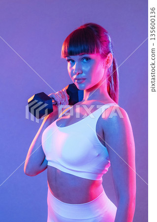 Arms exercise using dumbbell. Young sportive woman is in the studio 135600136