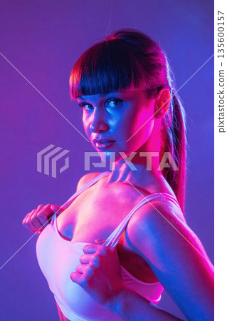 Touching the top, neon lighting. Young sportive woman is in the studio Touching the top, neon lighting. Young sportive woman is in the studio 135600157