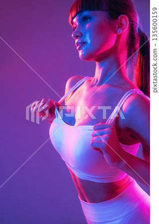 Neon lighting, showing the top. Young sportive woman is in the studio Neon lighting, showing the top. Young sportive woman is in the studio 135600159