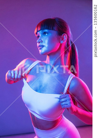 Neon lighting, showing the top. Young sportive woman is in the studio Neon lighting, showing the top. Young sportive woman is in the studio 135600162