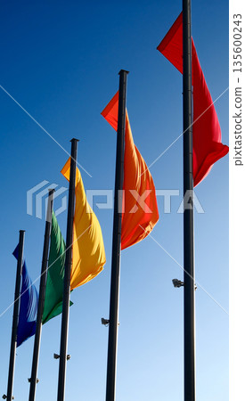 Colorful flags waving on tall poles against clear blue sky 135600243