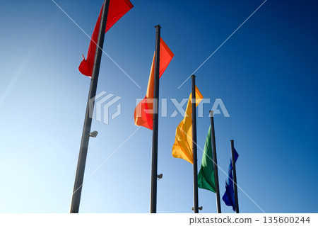 Colorful flags waving on tall poles against clear blue sky Colorful flags waving on tall poles against clear blue sky 135600244