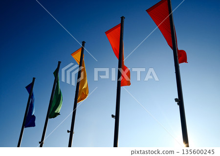 Colorful flags waving on tall poles against clear blue sky 135600245